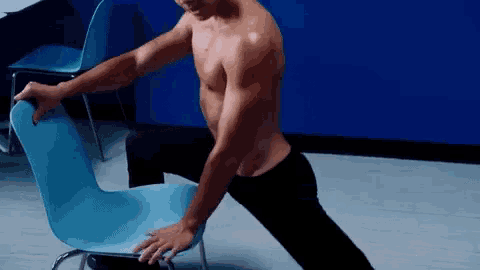 a shirtless man sits on a blue chair stretching his legs