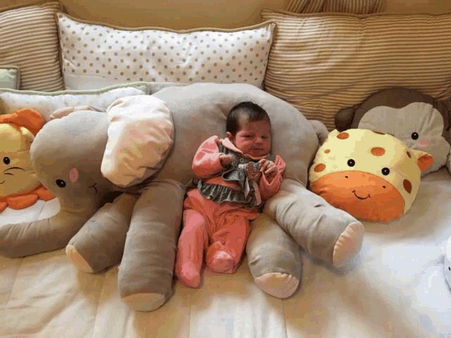 a baby laying on a bed with stuffed animals including an elephant and a giraffe