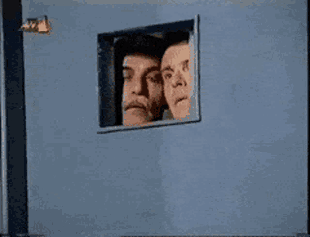 two men are looking out of a small window on a blue wall ..