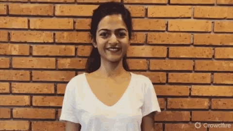 a woman in a white t-shirt is smiling in front of a brick wall .