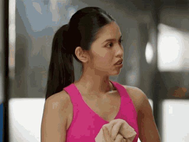 a woman in a pink tank top is holding a towel in her hand .