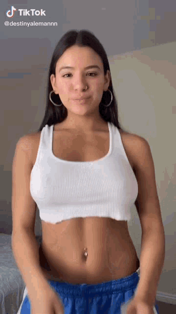 a woman in a white crop top and blue shorts is standing in a room .