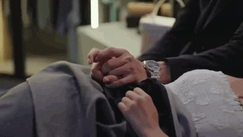 a man is holding a woman 's hand while laying on a bed .