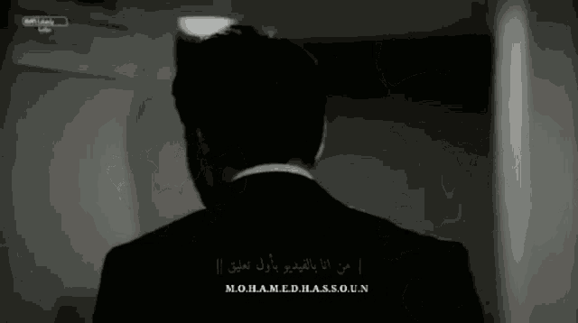 a man in a suit stands in a dark room with arabic writing on the bottom