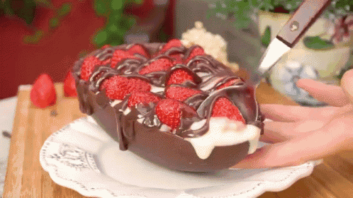 a person is taking a piece of chocolate cake with strawberries and chocolate icing .