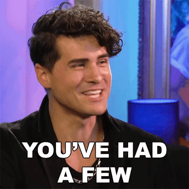 a man with curly hair is smiling and says " you 've had a few "