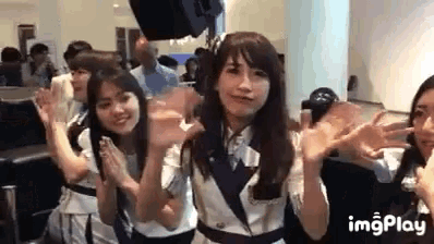 a group of young women are standing next to each other waving their hands in a room .