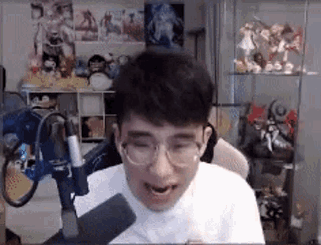 a man with glasses is sitting in front of a microphone in a room .