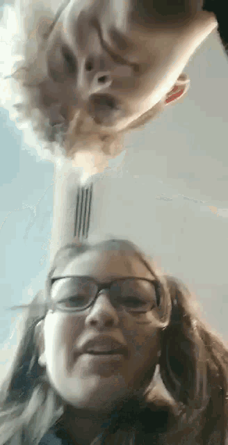 a boy and a girl are looking up at the camera . the girl is wearing glasses and pigtails .