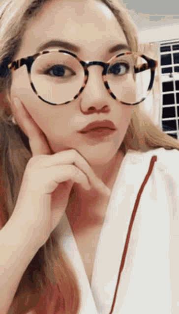a woman wearing glasses and a white shirt looks at the camera