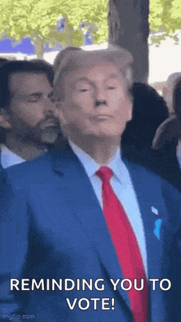 a man in a suit and tie is standing in front of a crowd and making a funny face .