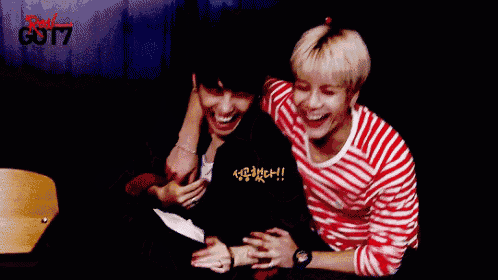 two young men are sitting next to each other and laughing in front of a sign that says got7 on it