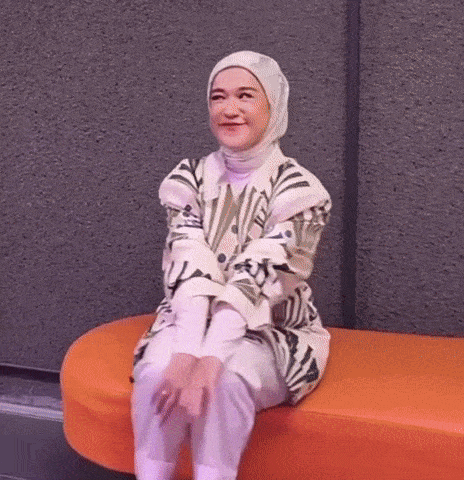 a woman wearing a hijab is sitting on an orange bench and smiling .