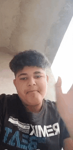 a young man with curly hair is wearing a black t-shirt and waving .
