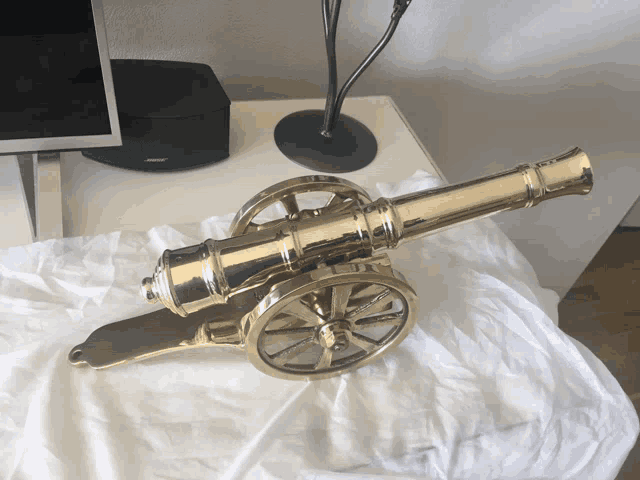 a brass cannon is sitting on a white cloth on a table next to a bose speaker