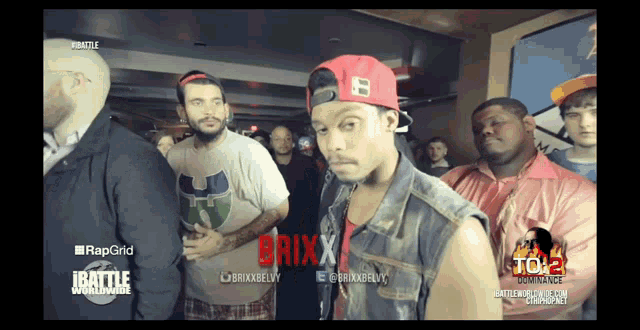 a man in a red hat stands in front of a group of people with the word brixx on his shirt