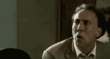 a man in a suit and tie is making a funny face while sitting at a table .