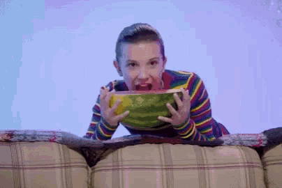a young girl is laying on a couch eating a large watermelon .