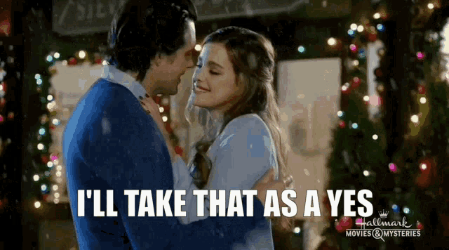 a man and a woman are hugging in front of christmas lights and the man is saying i 'll take that as a yes