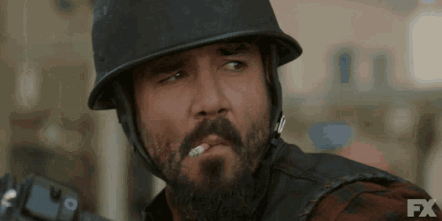 a man with a beard wearing a helmet and smoking a cigarette with fx written on the bottom