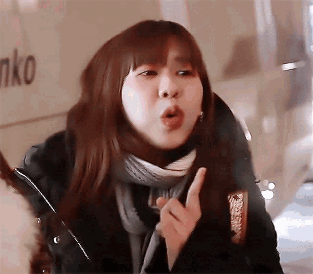 a woman wearing a scarf and a jacket is making a funny face in front of a sign that says nko