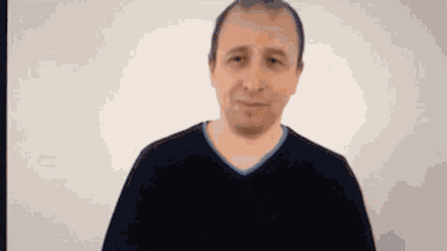 a man in a black sweater with a blue collar is looking at the camera