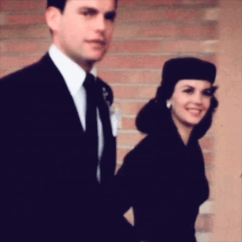 a man and a woman standing next to each other in front of a brick wall