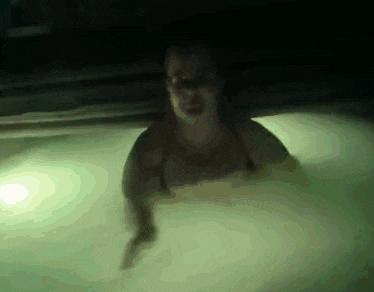 a woman is swimming in a pool with a green light behind her