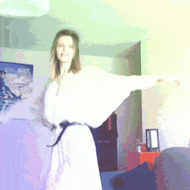 a woman in a white dress is dancing in a room with a poster on the wall that says across
