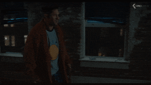 a man in a robe and a golden state warriors shirt stands in front of a window with kinocheck written on the bottom