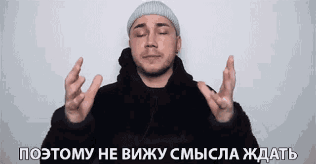a man in a beanie is making a funny face with his eyes closed and his hands in the air .