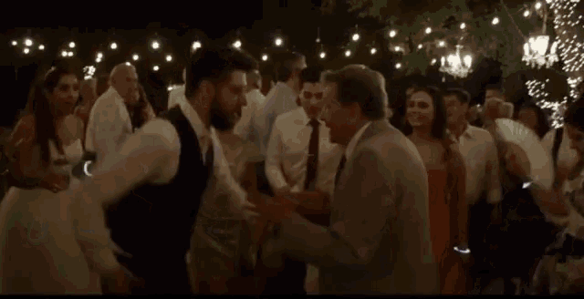 a group of people are dancing at a wedding reception under a string of lights .