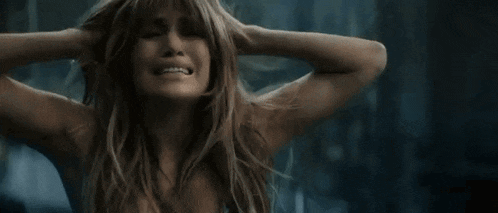 a woman is screaming and covering her ears in front of a wall of broken glass