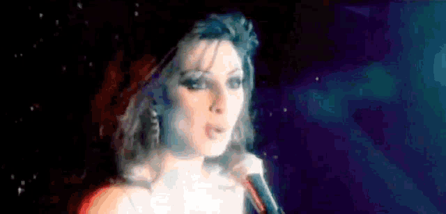 a woman is singing into a microphone in a dark room in front of a blue background .