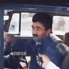 a man with a mustache is sitting in a car with a microphone in his hand .