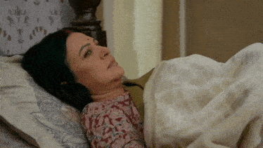 a woman is laying in bed with a blanket on