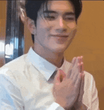 a young man in a white shirt is clapping his hands together .