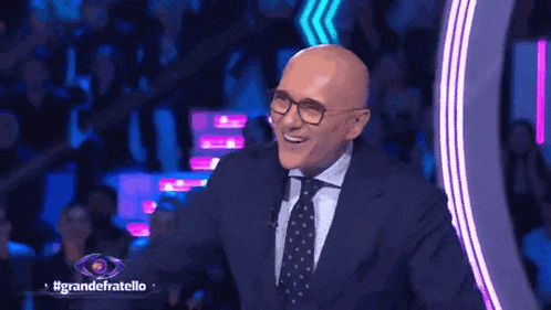 a bald man in a suit and tie is smiling in front of a crowd of people .