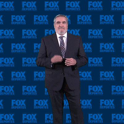a man in a suit and tie is standing in front of a fox deportes wall