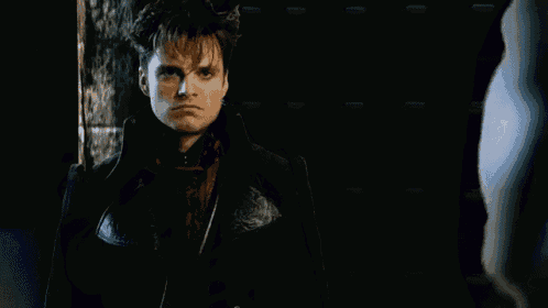 a man in a black coat is making a funny face while standing in the dark .