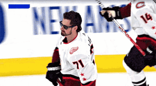 a hockey player wearing a number 71 jersey stands on the ice