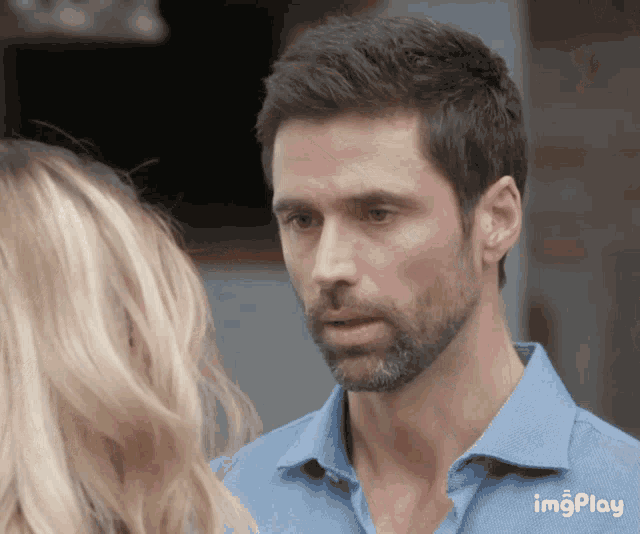 a man with a beard is looking at a woman while wearing a blue shirt