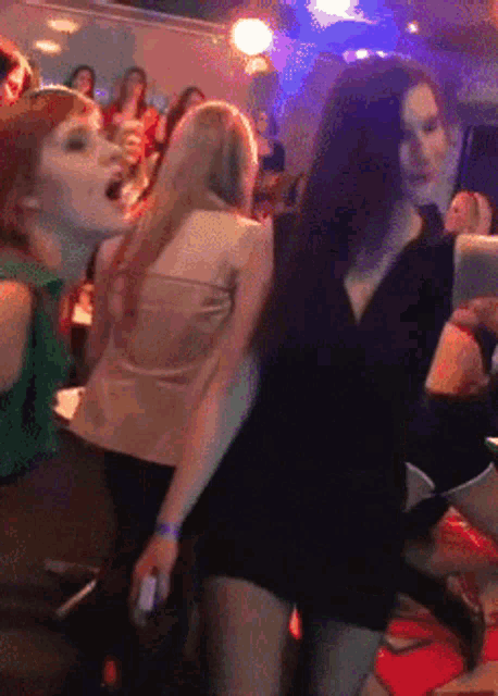 a group of women are dancing in a room with a man holding a cell phone