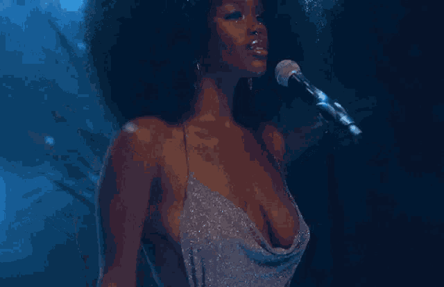 a woman with an afro is singing into a microphone in a very revealing dress .