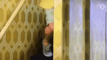 a person is standing in a corner of a room with a yellow wall and a white curtain .