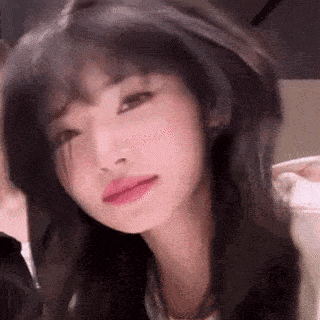 a close up of a woman 's face with a blurred background . she has long black hair and pink lips .