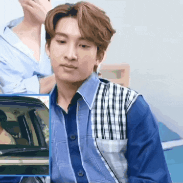 a young man in a blue shirt and plaid vest is sitting in a car .