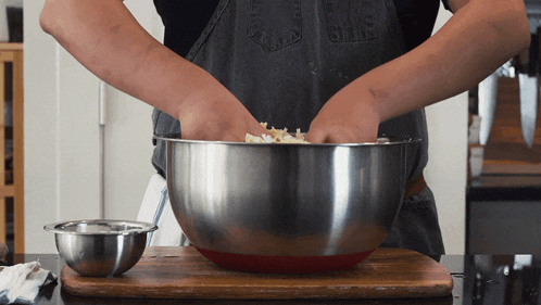 a person in an apron is mixing something in a large metal bowl
