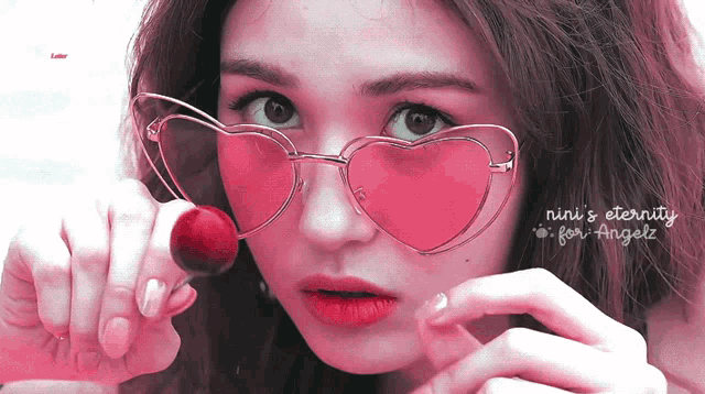 a woman wearing pink heart shaped sunglasses holds a cherry