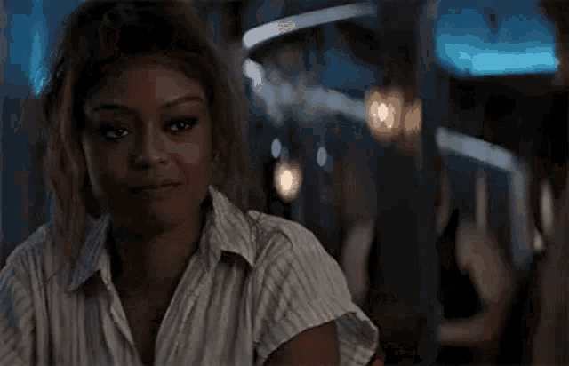 a woman in a striped shirt is sitting at a table in a bar .